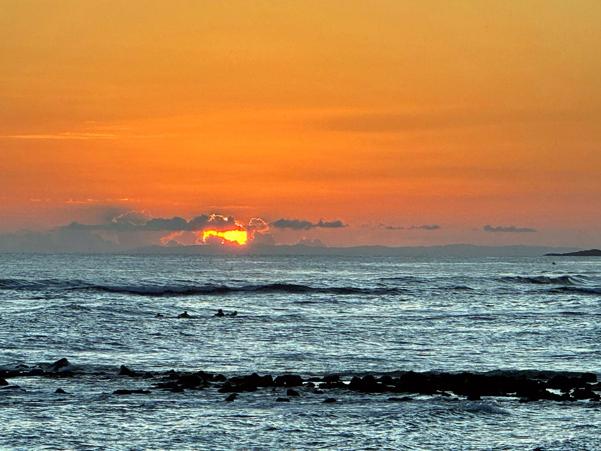 An orange sunset over the water with surfers in the lineup